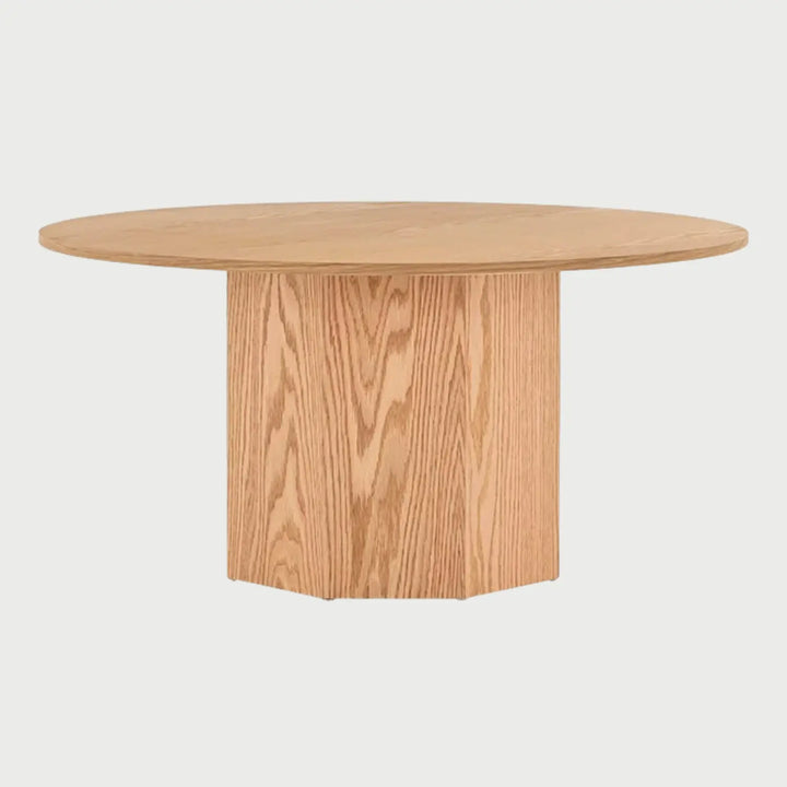 Vista frontal de la mesa de centro circular Aida en color beige encino; presenta una superficie redonda delgada soportada por una base cilíndrica central de gran volumen que muestra la veta natural de la madera.