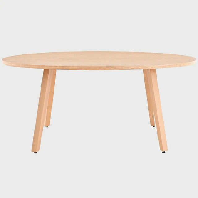 Vista frontal de la mesa de comedor ovalada Xocos en color beige encino; el acabado en madera clara realza las líneas curvas de la cubierta y la solidez de su estructura de soporte.