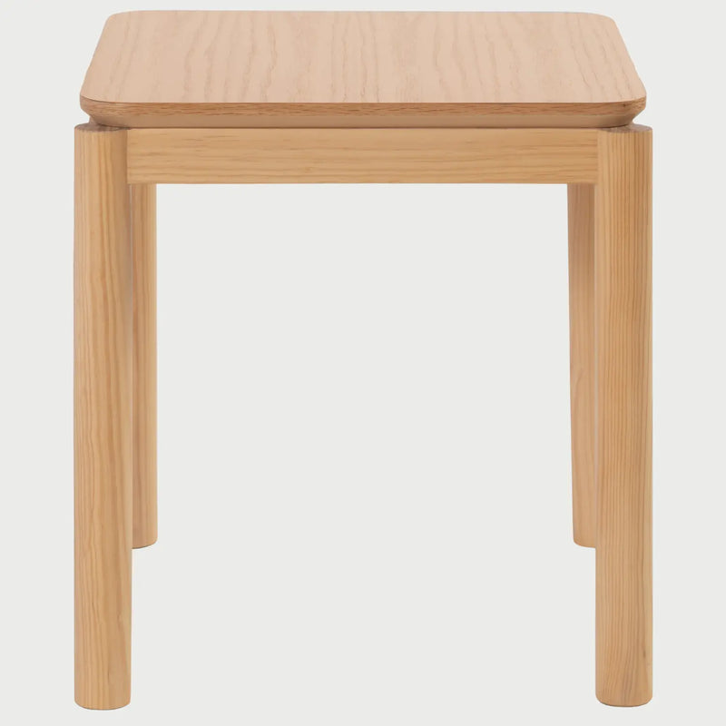 Vista frontal de la mesa lateral Akari de 50 cm; presenta una superficie cuadrada de bordes redondeados y cuatro patas cilíndricas robustas en madera de encino con acabado natural beige.