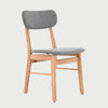 Vista lateral de la silla Marcela en color gris, mostrando el perfil delgado del respaldo de madera y la estructura de soporte reforzada bajo el asiento en acabado encino.