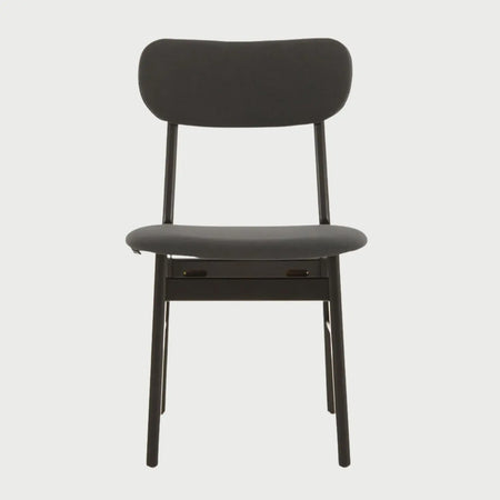 Vista frontal de la silla Marcela en color negro integral, con un respaldo ovalado horizontal, asiento acolchado tapizado y estructura de patas cilíndricas de madera en acabado negro mate.