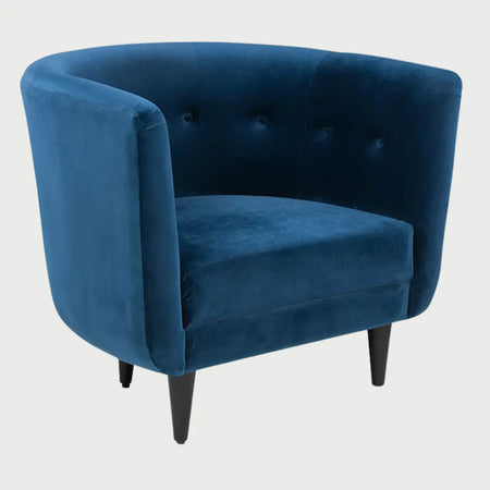 Vista lateral del sillón Tavari GAIA en terciopelo azul, mostrando su estructura semicircular envolvente, el detalle de botones decorativos en el respaldo interior y las patas delgadas en color negro.