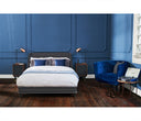 Sillón Tavari GAIA tapizado en terciopelo azul, con respaldo curvo, ubicado junto a una cama en un ambiente acogedor.
