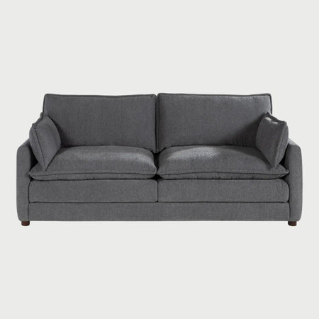 Vista frontal del sofá Andrea GAIA de tres cuerpos en tela gris, que muestra tres amplios cojines de asiento y respaldo con diseño acolchado tipo "puffy", descansabrazos rectos y patas de madera discretas.