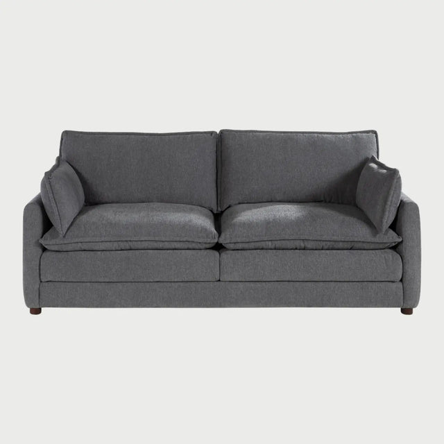 Vista frontal del sofá Andrea GAIA de tres cuerpos en tela gris, que muestra tres amplios cojines de asiento y respaldo con diseño acolchado tipo "puffy", descansabrazos rectos y patas de madera discretas.