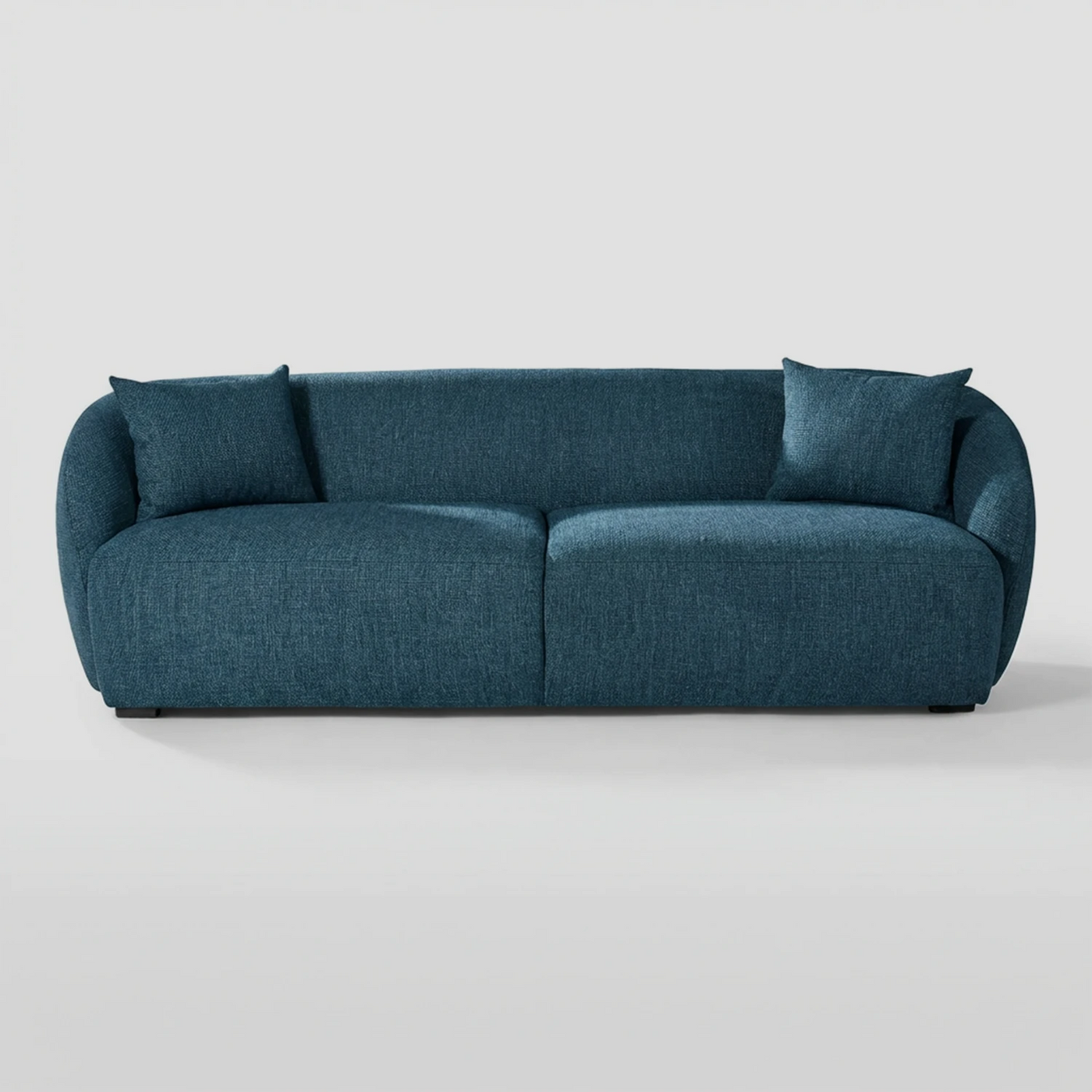 Vista frontal del sofá Kant GAIA de tres cuerpos en tela azul, destacando su diseño de proporciones generosas con formas redondeadas, brazos integrados envolventes y cojines decorativos a juego.