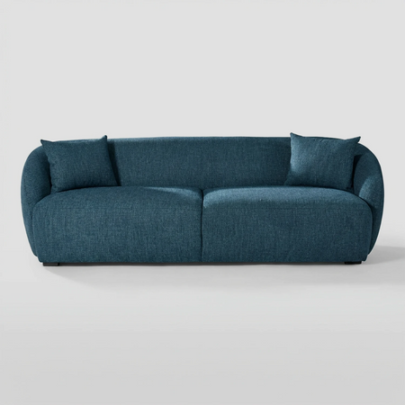 Vista frontal del sofá Kant GAIA de tres cuerpos en tela azul, destacando su diseño de proporciones generosas con formas redondeadas, brazos integrados envolventes y cojines decorativos a juego.
