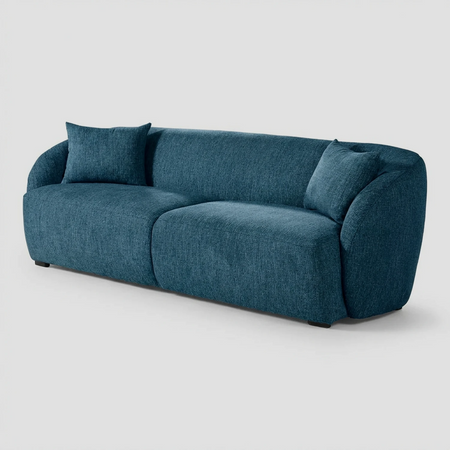 Vista lateral del sofá Kant azul de tres cuerpos, resaltando el perfil curvo continuo que une el respaldo con los descansabrazos y su estructura de bajo impacto visual.