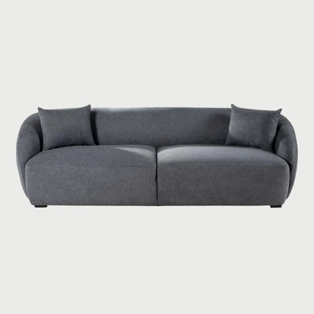 Vista frontal del sofá Kant de tres cuerpos en color gris oscuro, destacando la elegancia de su tejido de trama cerrada y sus líneas fluidas sin aristas pronunciadas.