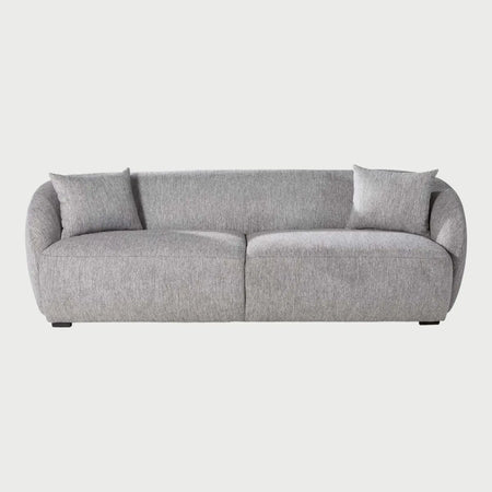 Vista frontal del sofá Kant de tres cuerpos en color gris claro, resaltando su silueta moderna y acogedora con cojines mullidos y una base sólida de bajo perfil.