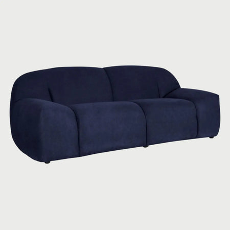 Vista lateral del sofá Marcus azul, resaltando su silueta baja y el grosor de su estructura acolchada que proporciona una estética moderna y de máximo confort.