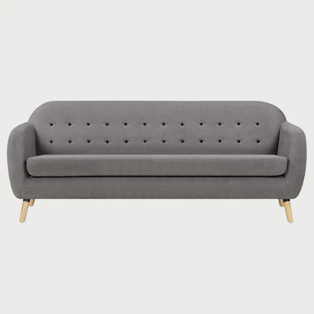 Vista frontal del sofá San Blas de tres cuerpos en color gris claro, resaltando el detalle de los botones en el respaldo y la ligereza visual de la base de madera clara.