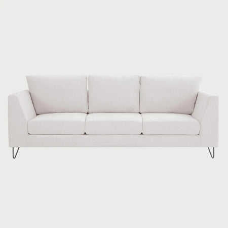 Vista frontal del sofá Yoco de tres cuerpos en tela blanca, con tres cojines de respaldo, tres cojines de asiento y patas de madera en acabado negro que aportan un contraste moderno y minimalista.