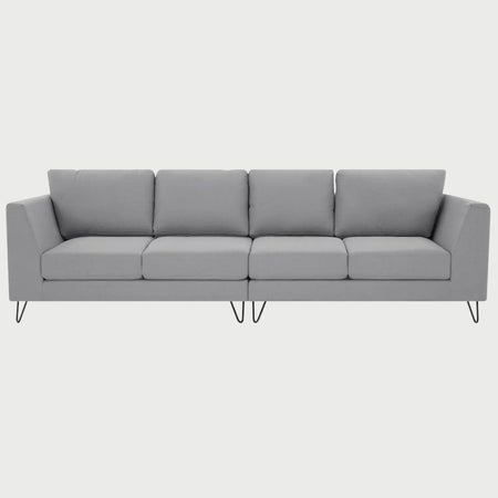 Vista frontal del sofá Yoco de cuatro plazas en color gris, destacando la amplitud de su superficie de descanso y el soporte sofisticado de sus patas en acabado nogal.