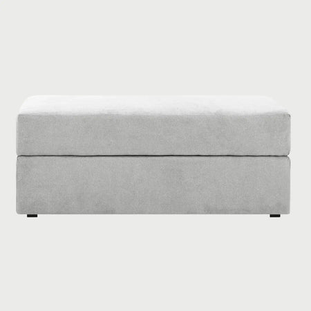 Vista frontal del taburete Amil en color gris, resaltando su versatilidad para integrarse en ambientes modernos como asiento auxiliar o reposapiés.