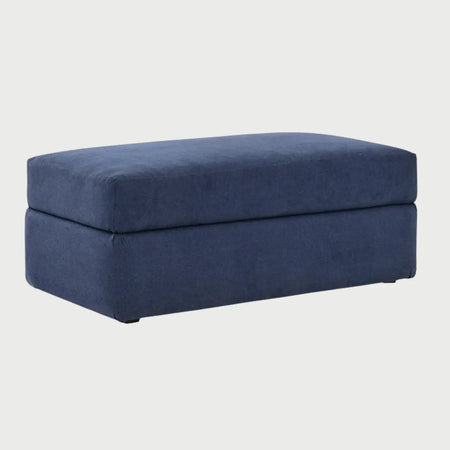 Vista lateral del taburete Amil azul, mostrando su perfil rectangular uniforme y la costura perimetral que define su forma geométrica estable.