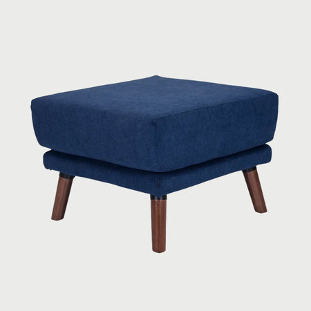 Vista lateral del taburete San Blas azul, mostrando el perfil robusto del acolchado y la inclinación de sus patas de madera nogal que aportan estabilidad y elegancia.