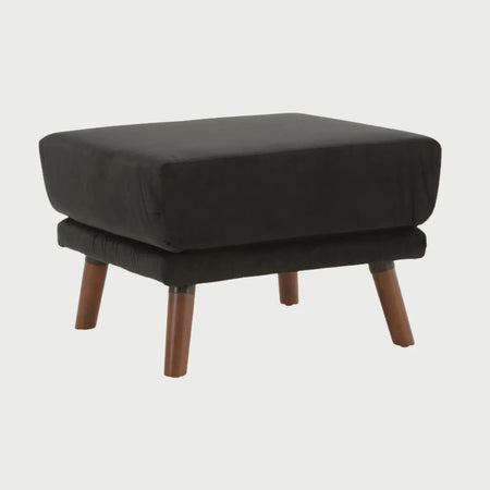 Vista lateral del taburete San Blas en terciopelo negro, mostrando el brillo sutil del tejido y la inclinación de sus patas de madera nogal que aportan un estilo sofisticado.